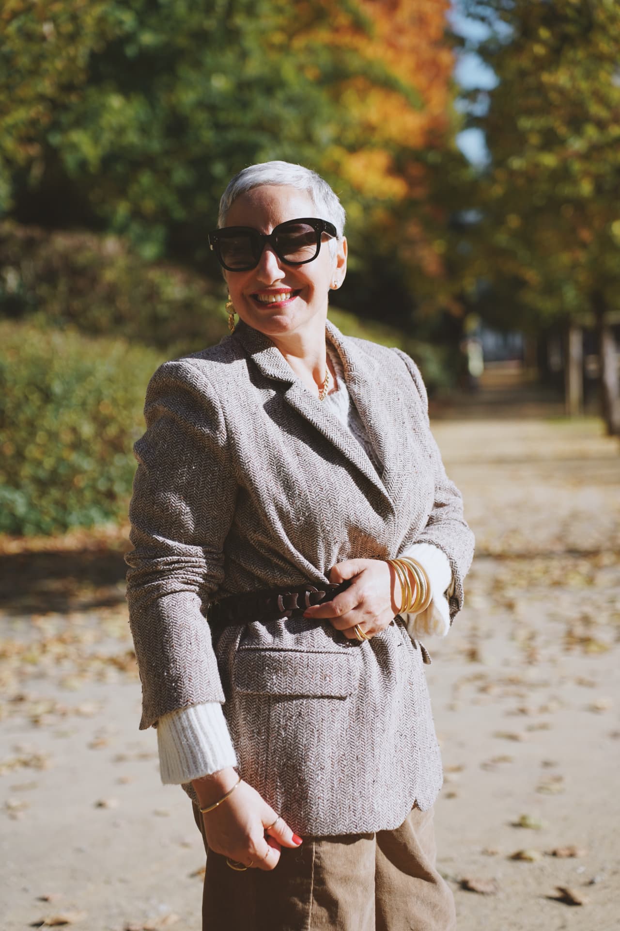 Blazer en tweed ceinturé, sourire dans l'allée du parc