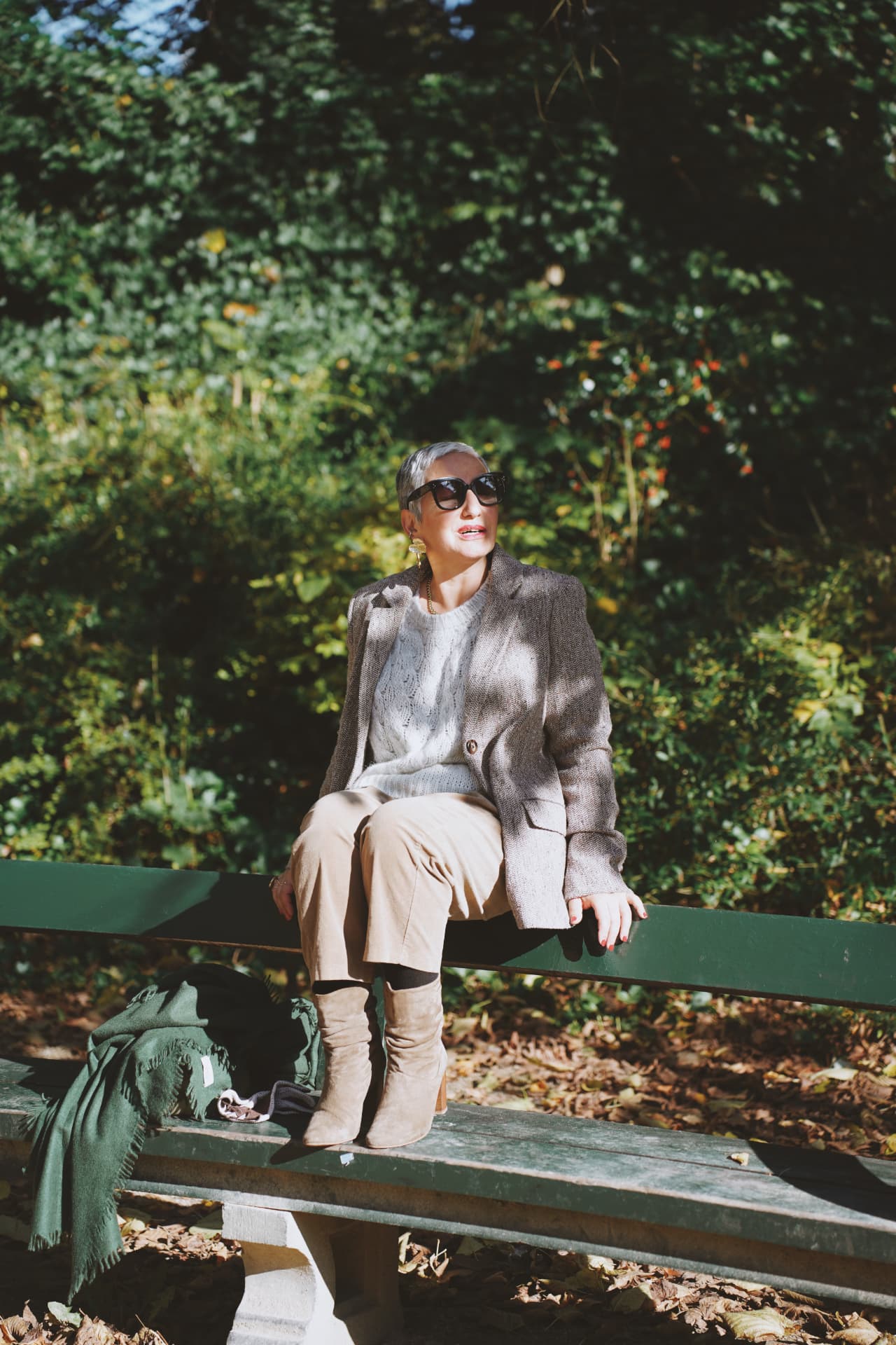 Assise sur le dossier d'un banc, blazer en tweed et bottes claires