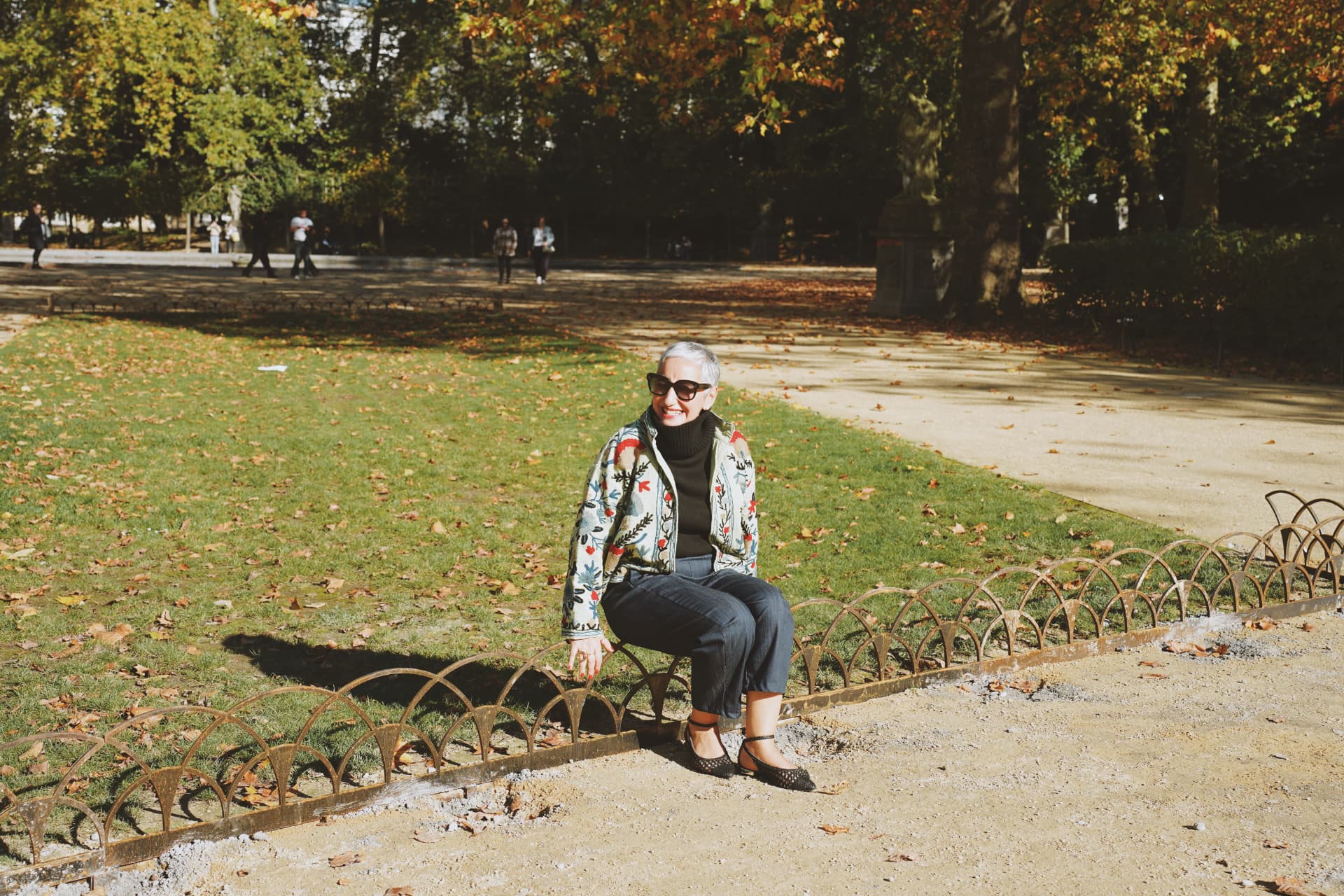 Assise sur la bordure du parterre, veste brodée florale dans le parc