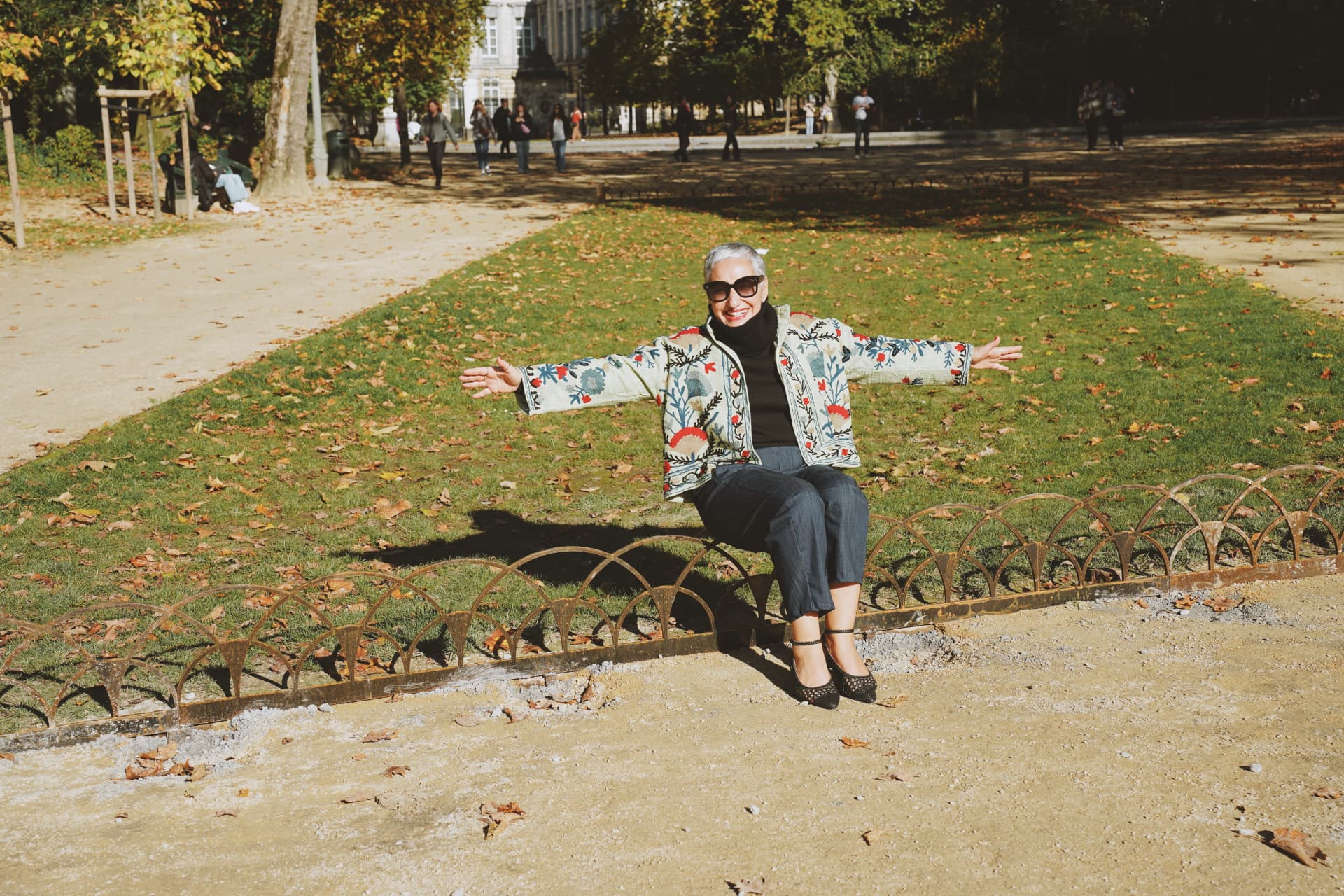Assise sur la bordure du parterre, bras ouverts, veste brodée florale