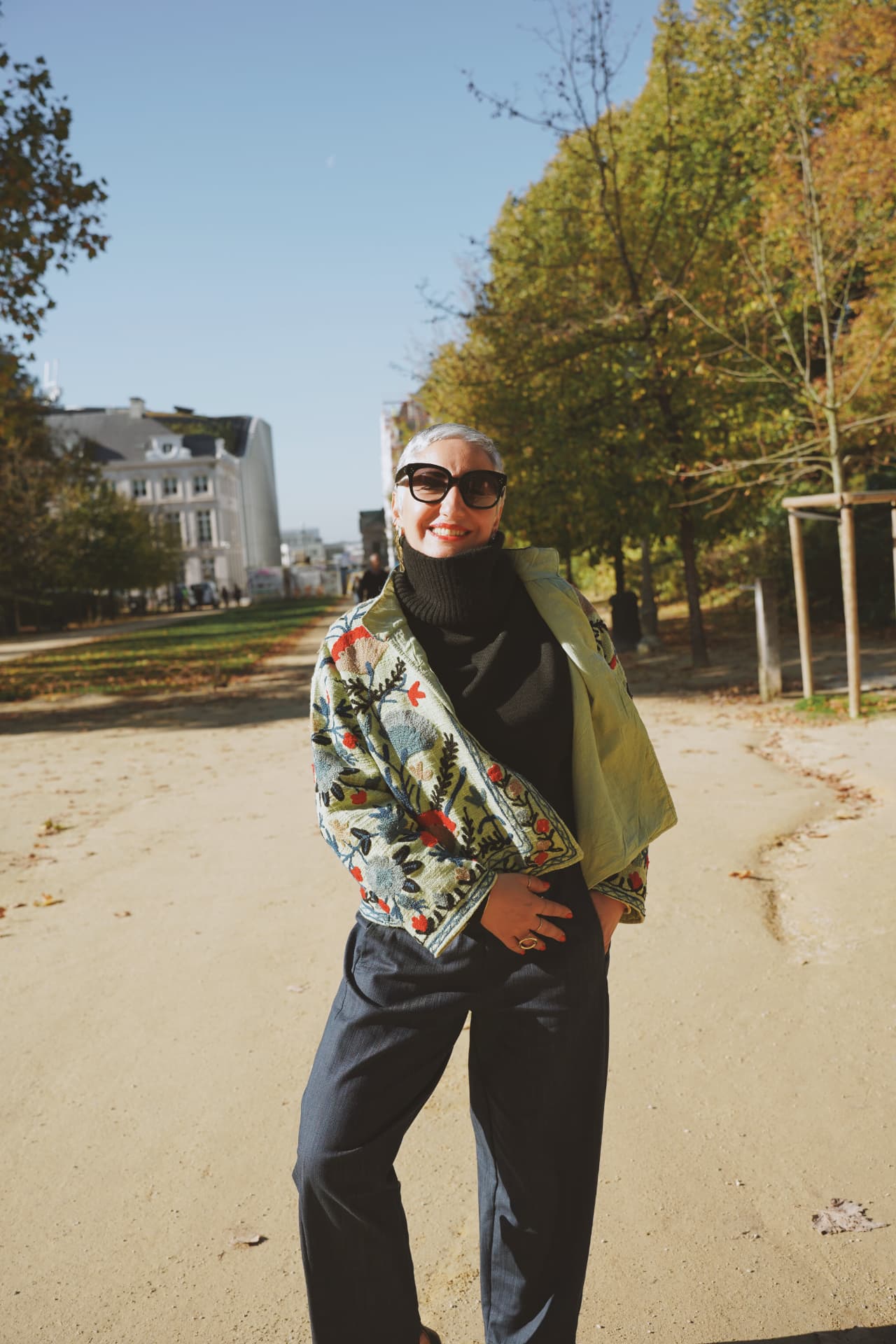 Silhouette souriante en veste brodée, allée d'un parc bruxellois