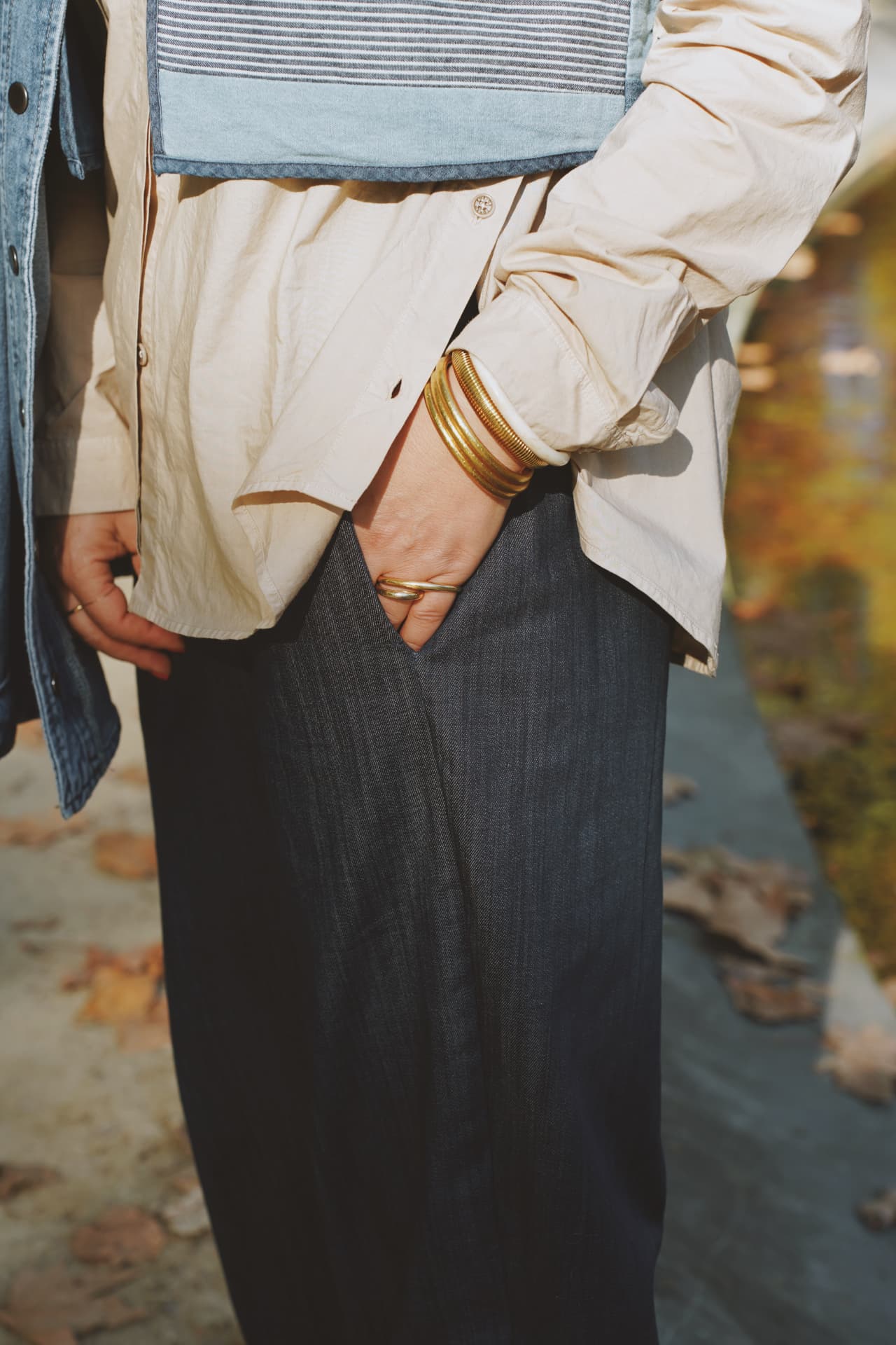 Détail : gilet patchwork denim, chemise écrue et bracelets dorés