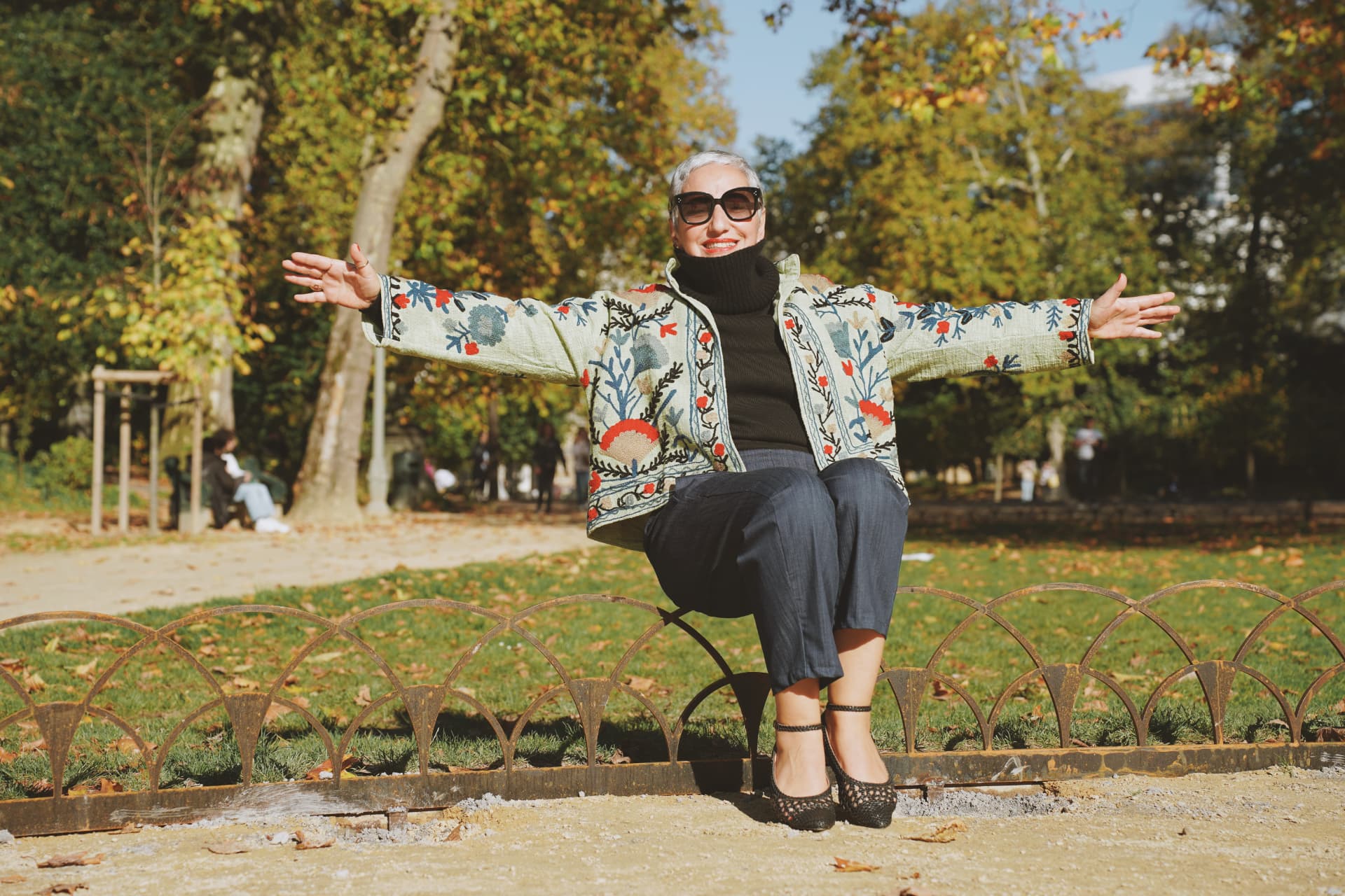 Bras ouverts, assise sur la bordure du parterre