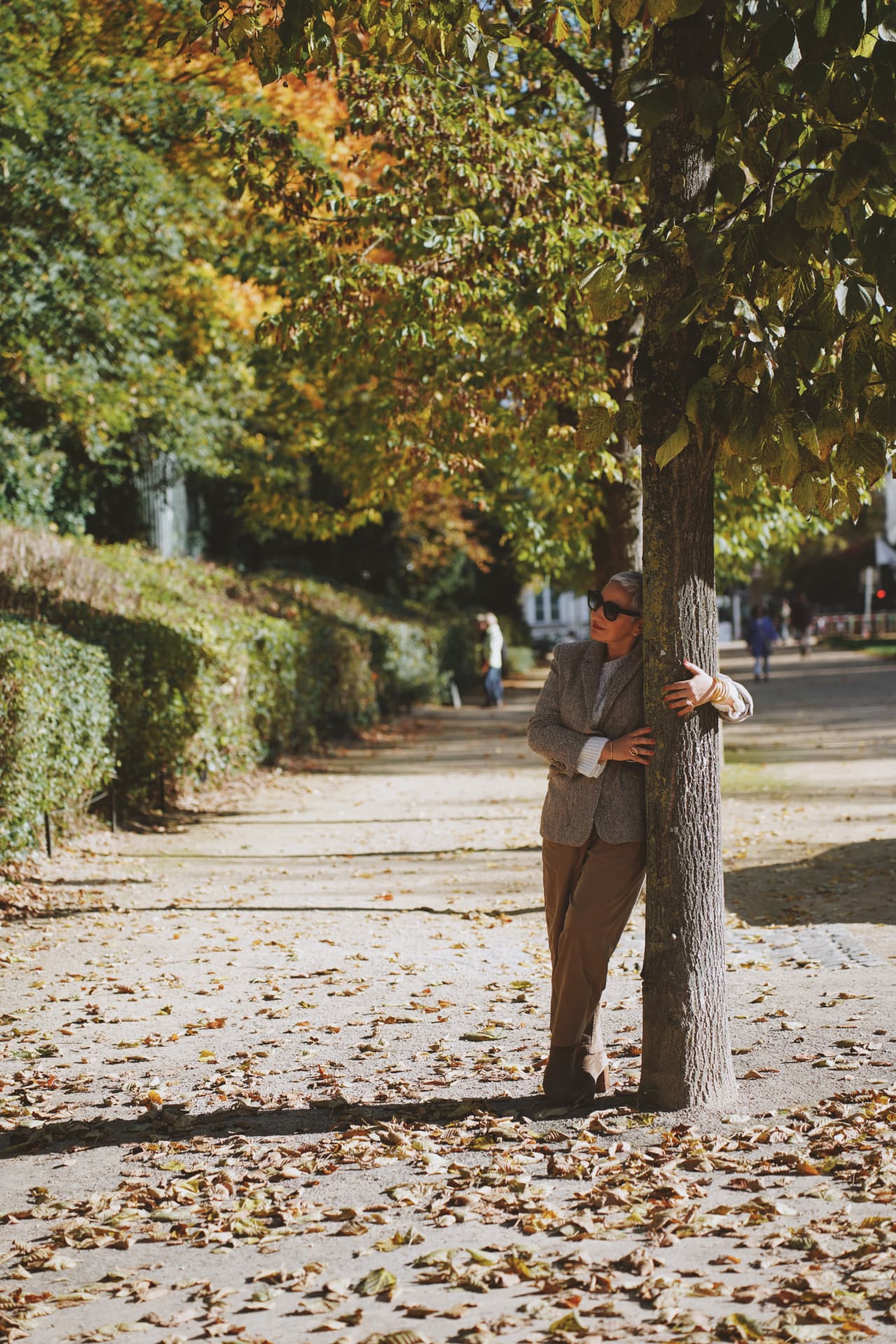 Adossée à un arbre de l'avenue, blazer en tweed et pantalon camel