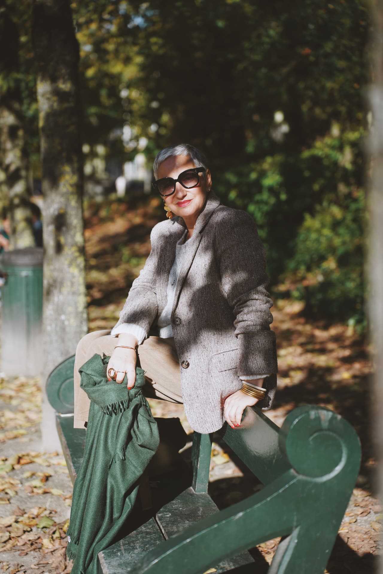 Assise sur le dossier d'un banc vert, blazer en tweed et plaid vert