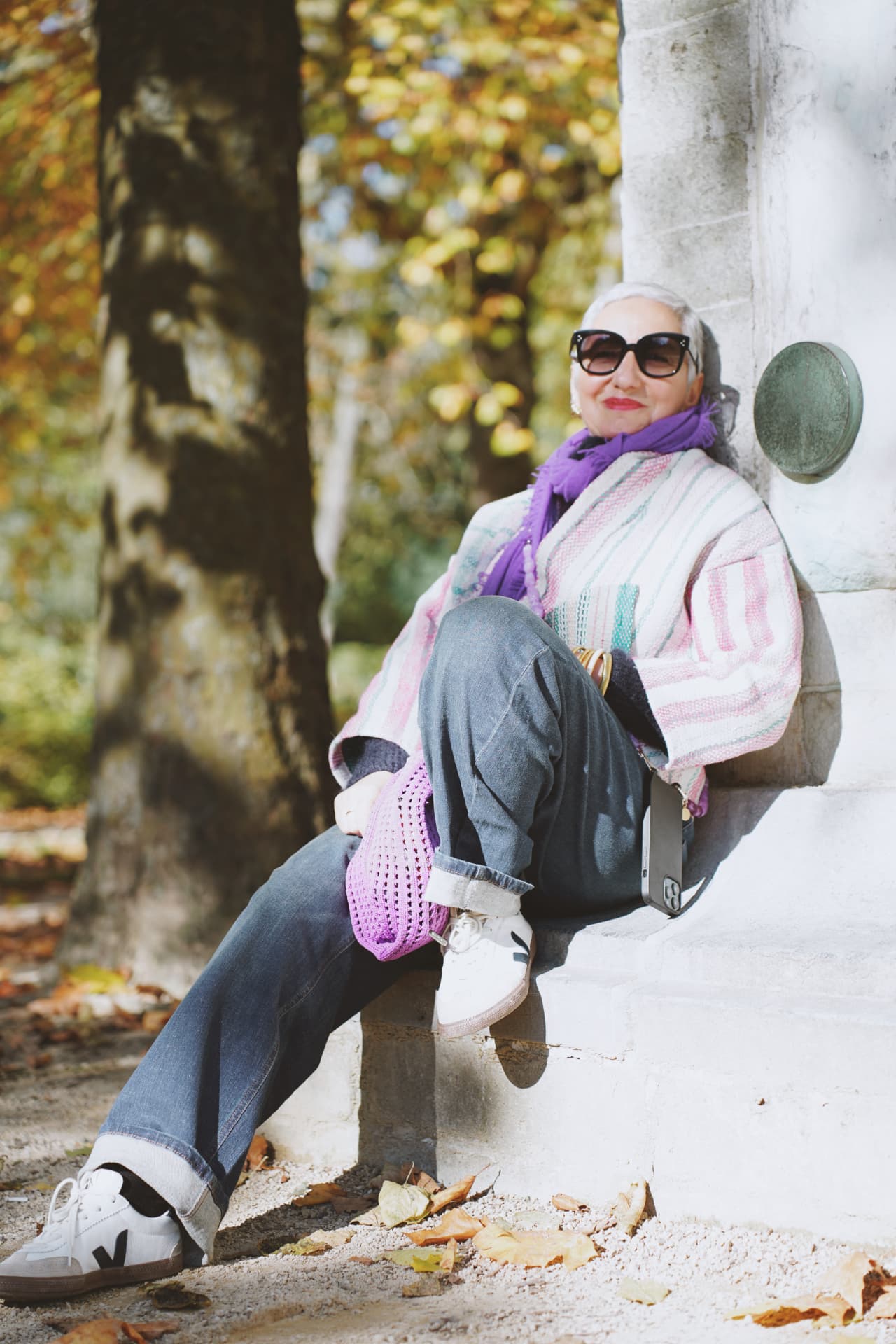 Poncho rayé et écharpe violette, assise sur un socle en pierre